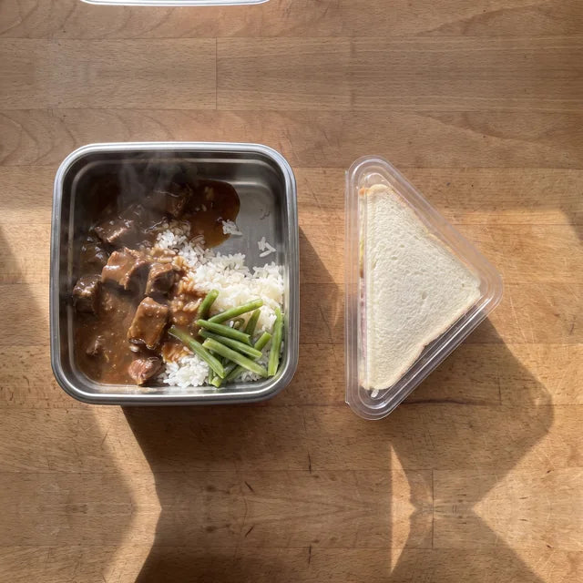 A hot meal in the stainless tray beside a shop-bought sandwich in its plastic wedge